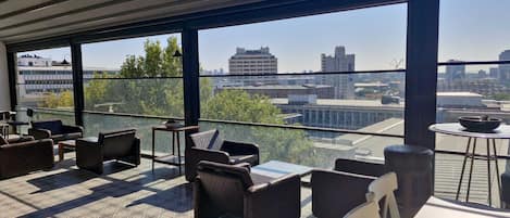 Un espacio moderno al aire libre con vistas a la ciudad, que incluye una variedad de sillas y mesas, y un panel de vidrio transparente.