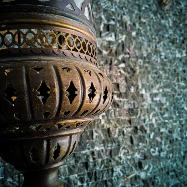 A close-up of a metal object with intricate cut-out patterns, set against a textured stone wall. - Cihan Palas (Ankara)