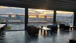 Eine Dachterrasse mit Blick auf die Stadt bei Sonnenuntergang, ausgestattet mit modernen Sitzgelegenheiten und einem gefliesten Boden.