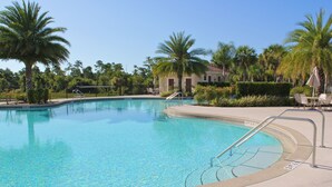 A clear swimming pool surrounded by palm trees and a building with a red roof. - Fantastic Townhome with Club Access, Steps from Walmart, and Close to Disney! (Kissimmee)