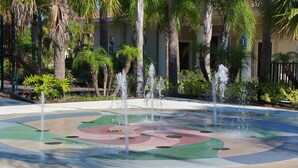 A circular water feature with multiple fountains, surrounded by palm trees and greenery. - Fantastic Townhome with Club Access, Steps from Walmart, and Close to Disney! (Kissimmee)