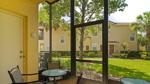 A covered patio with a table and chairs, overlooking a well-maintained lawn and a building with multiple windows and balconies. - Fantastic Townhome with Club Access, Steps from Walmart, and Close to Disney! (Kissimmee)
