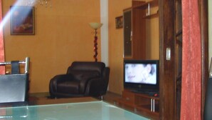 A living room with a leather sofa, a television, and a chandelier. - Falkenstein Aparts (Falkenstein/Vogtl.)