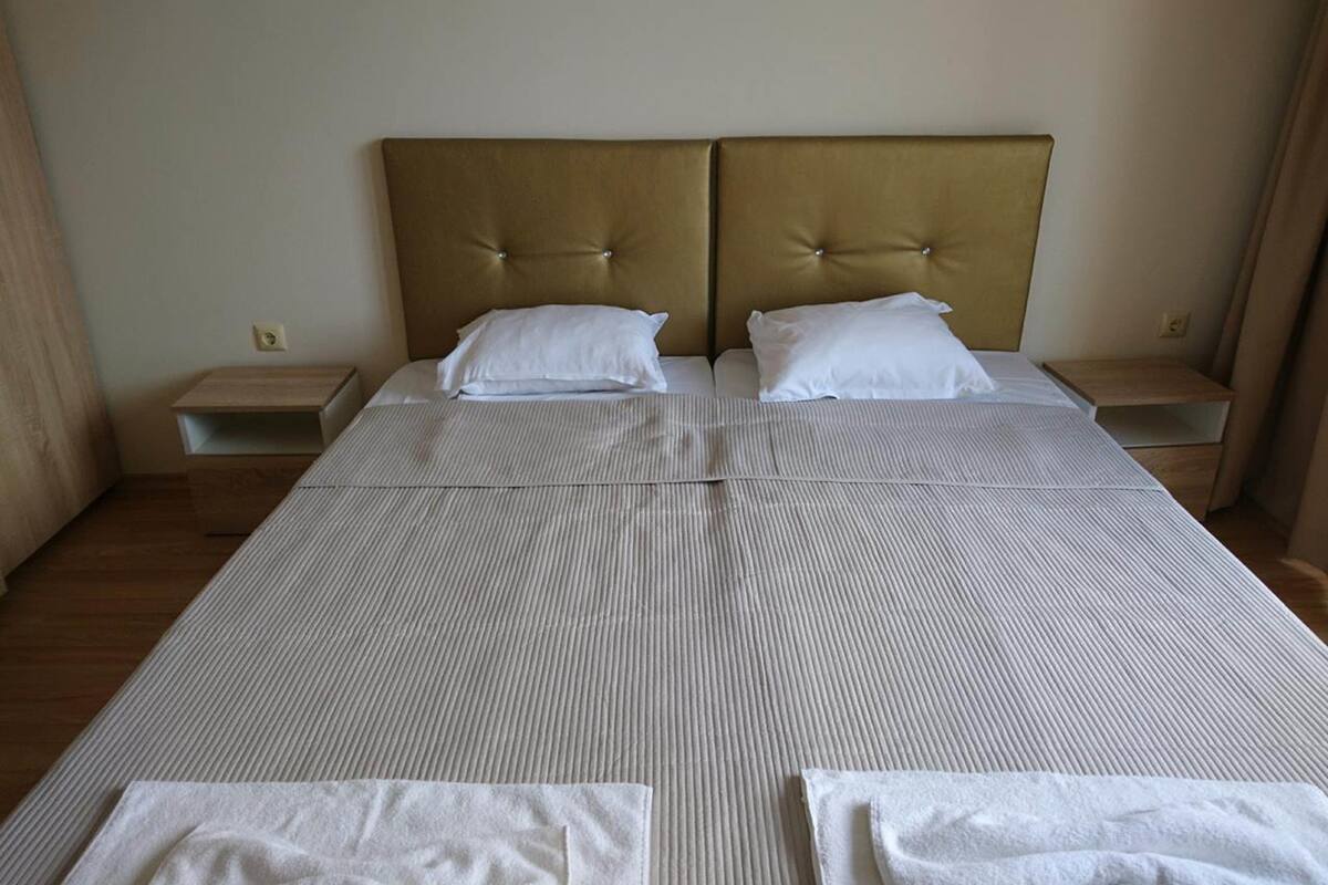 A double bed with a striped bedspread, two white pillows, and a tufted headboard. There are two bedside tables with lamps.