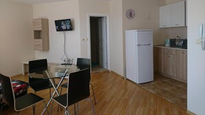 A compact kitchen with a refrigerator, a microwave, and a sink. There is a dining table with chairs and a television mounted on the wall. - Falkenstein Aparts (Falkenstein/Vogtl.)