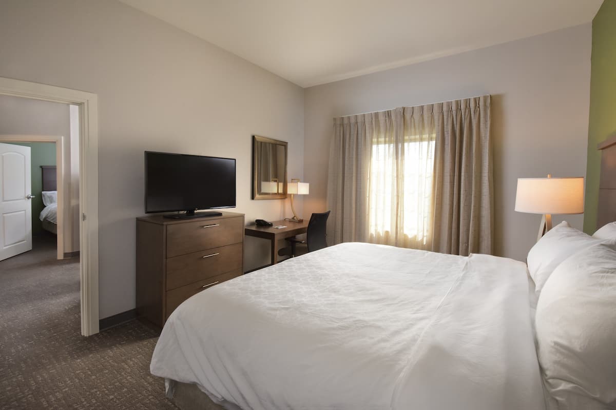 Ein Hotelzimmer mit einem Bett, einem Schreibtisch mit Stuhl, einem Fernseher, einer Lampe und einem Fenster mit Vorhängen.