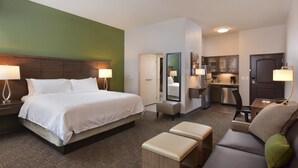 Quarto de hotel com cama grande, sofá, mesinha, área de cozinha e banheiro.