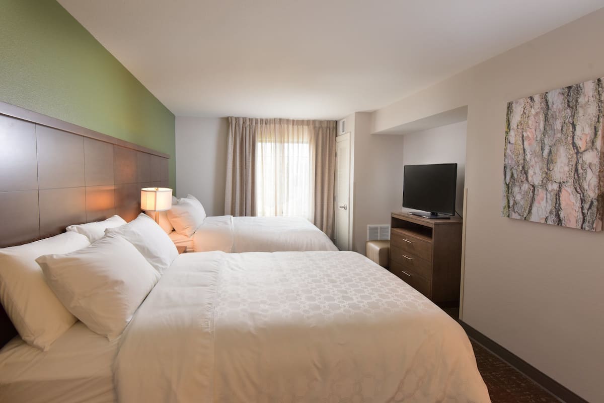 Ein Hotelzimmer mit zwei Betten, einem Fernseher, einem Schminktisch und einem Bild an der Wand.