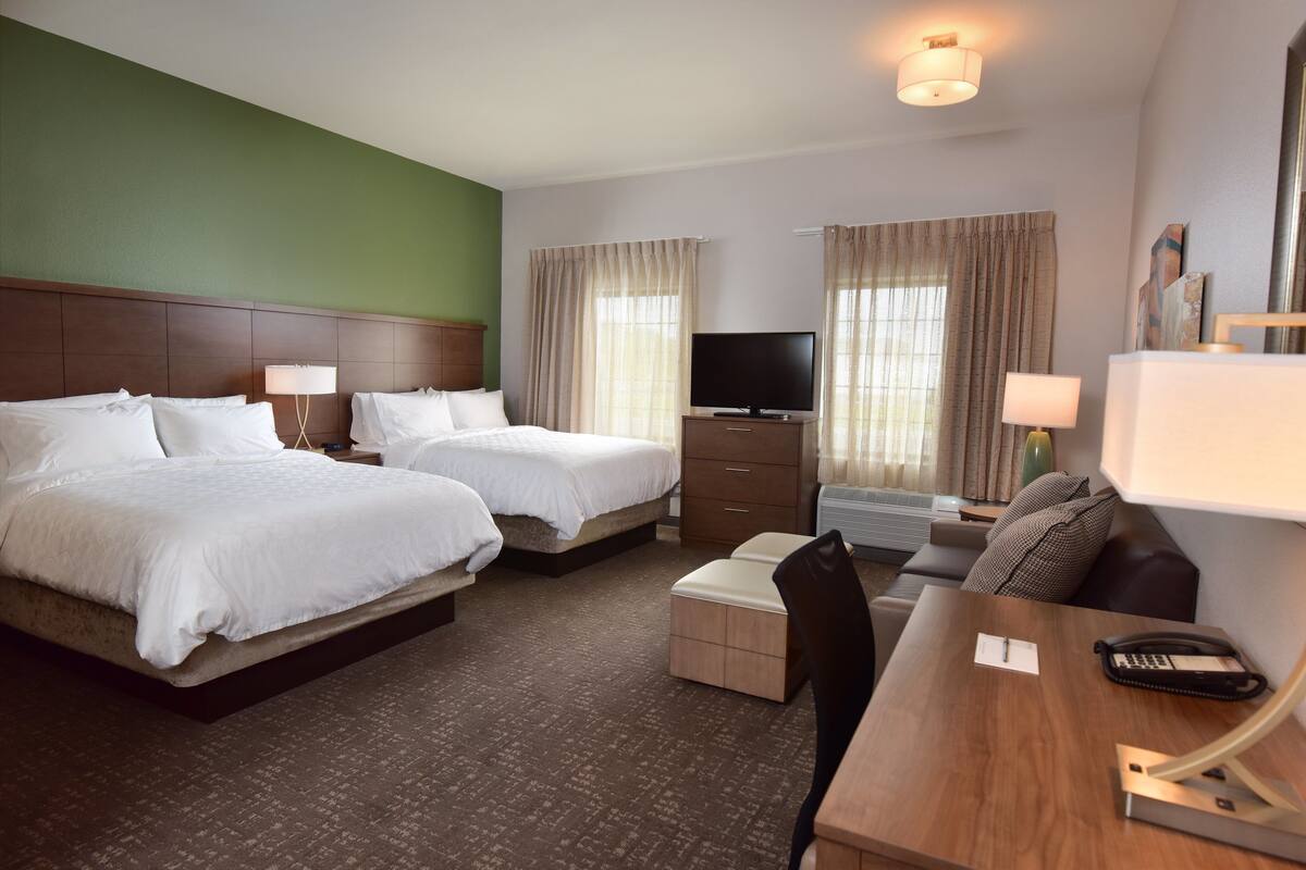 Ein Hotelzimmer mit zwei Betten, einem Schreibtisch mit Telefon, einem Fernseher und einem Sessel.