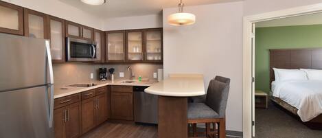 Habitación de hotel compacta con kitchenette, cama y un pequeño rincón de descanso.