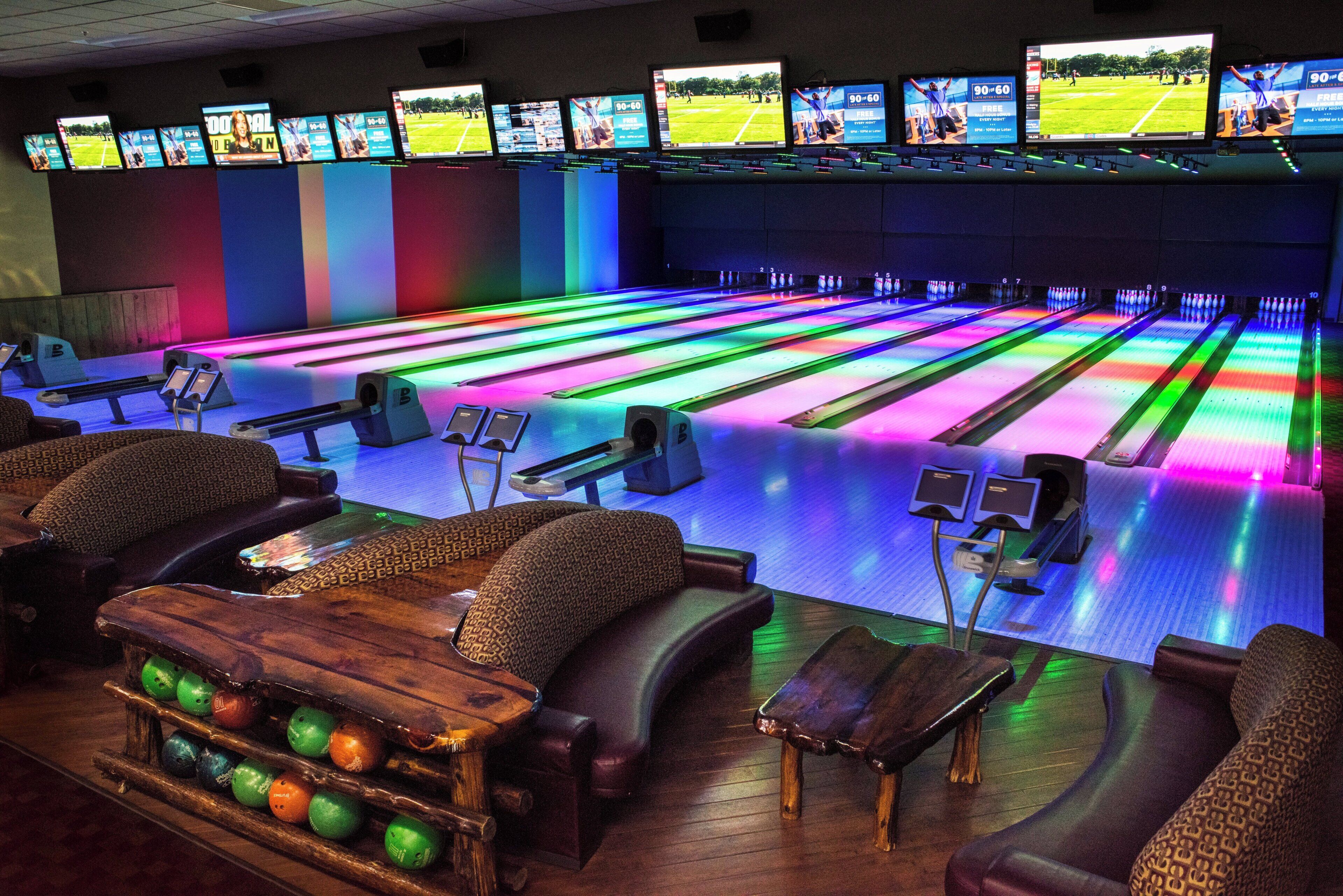 A bowling alley with multiple lanes, seating areas, and a bowling ball rack.