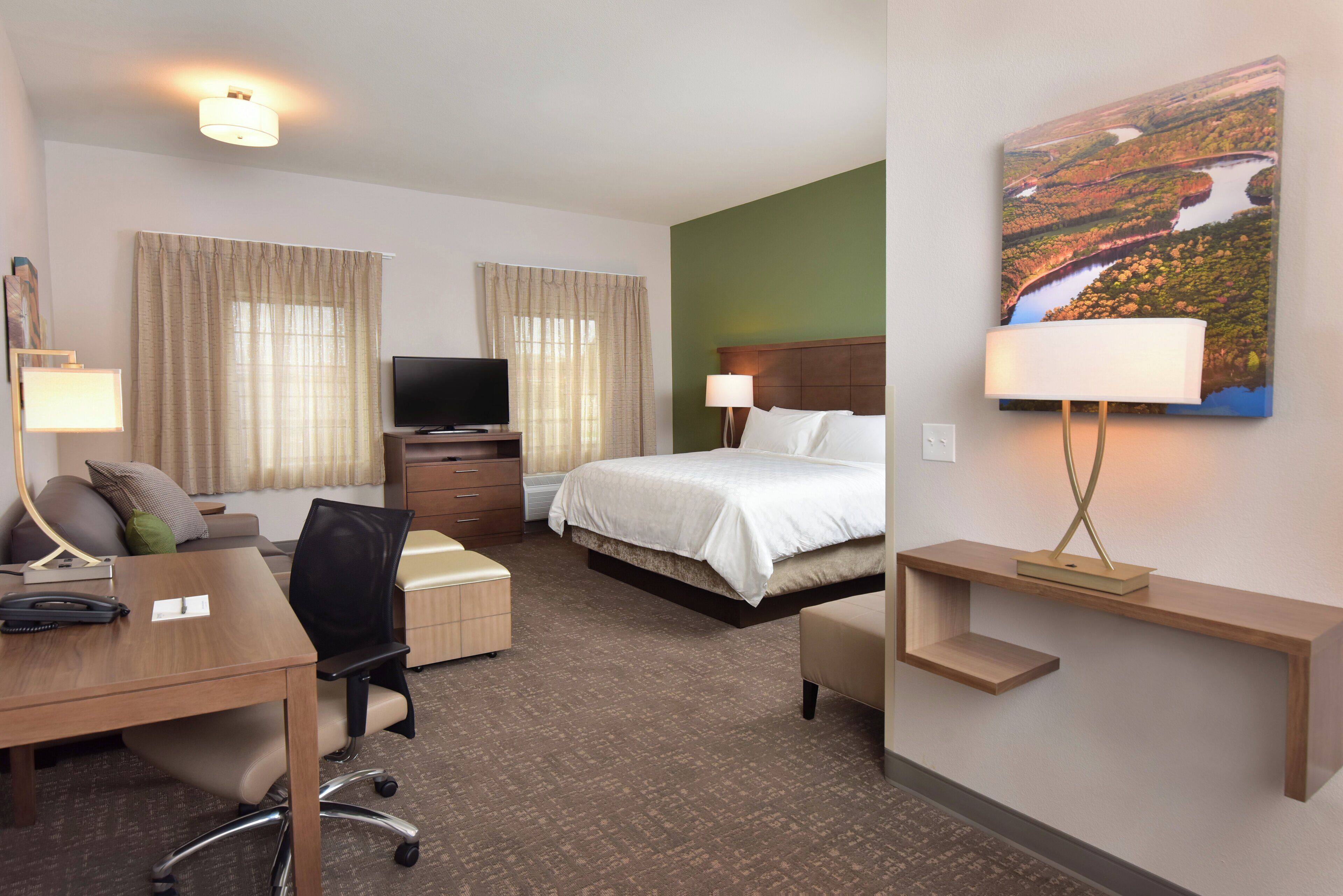 A hotel room with a bed, desk, chair, television, and a painting on the wall.