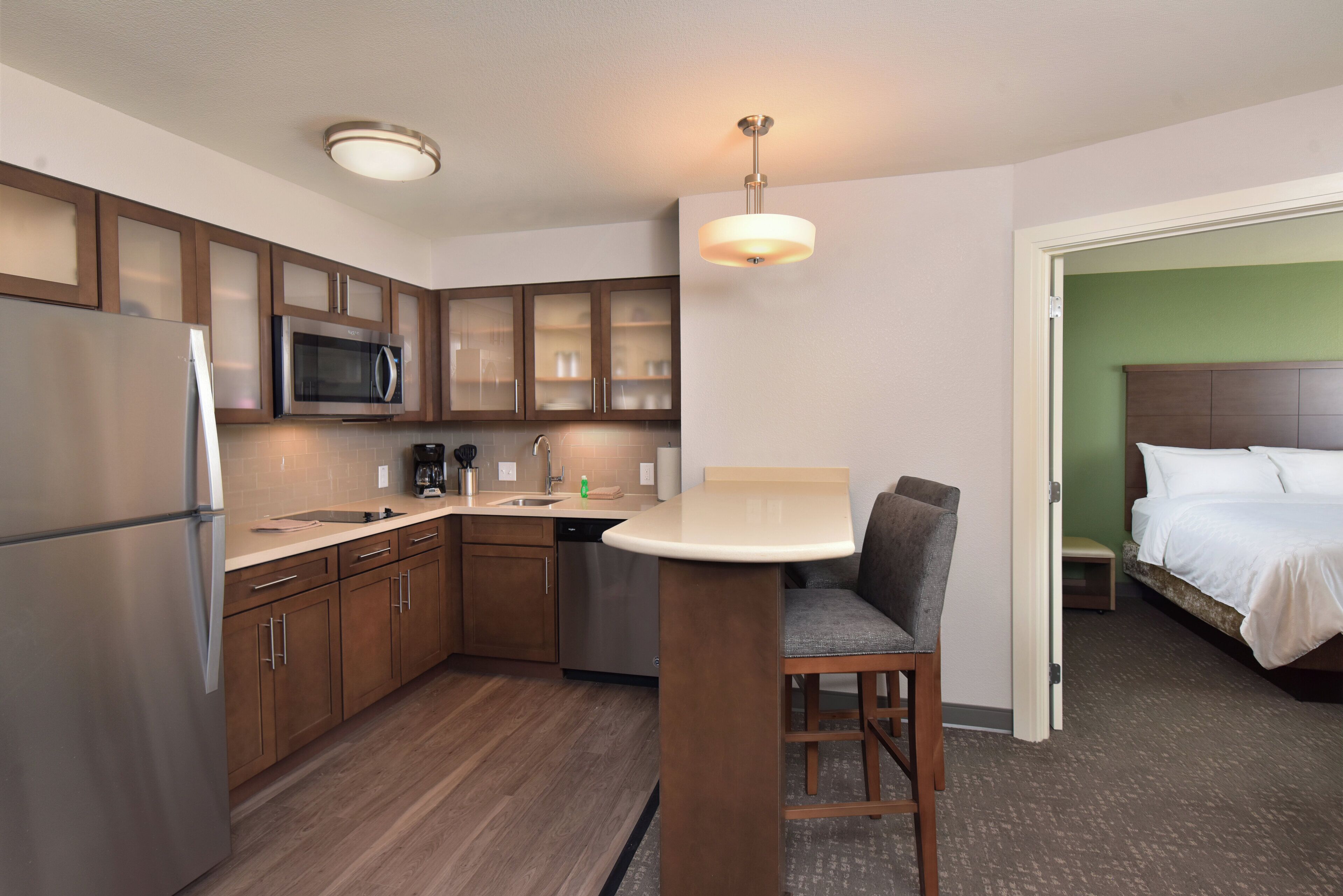 A compact kitchen with a refrigerator, microwave, and a sink. There's a bar stool and a small dining table.