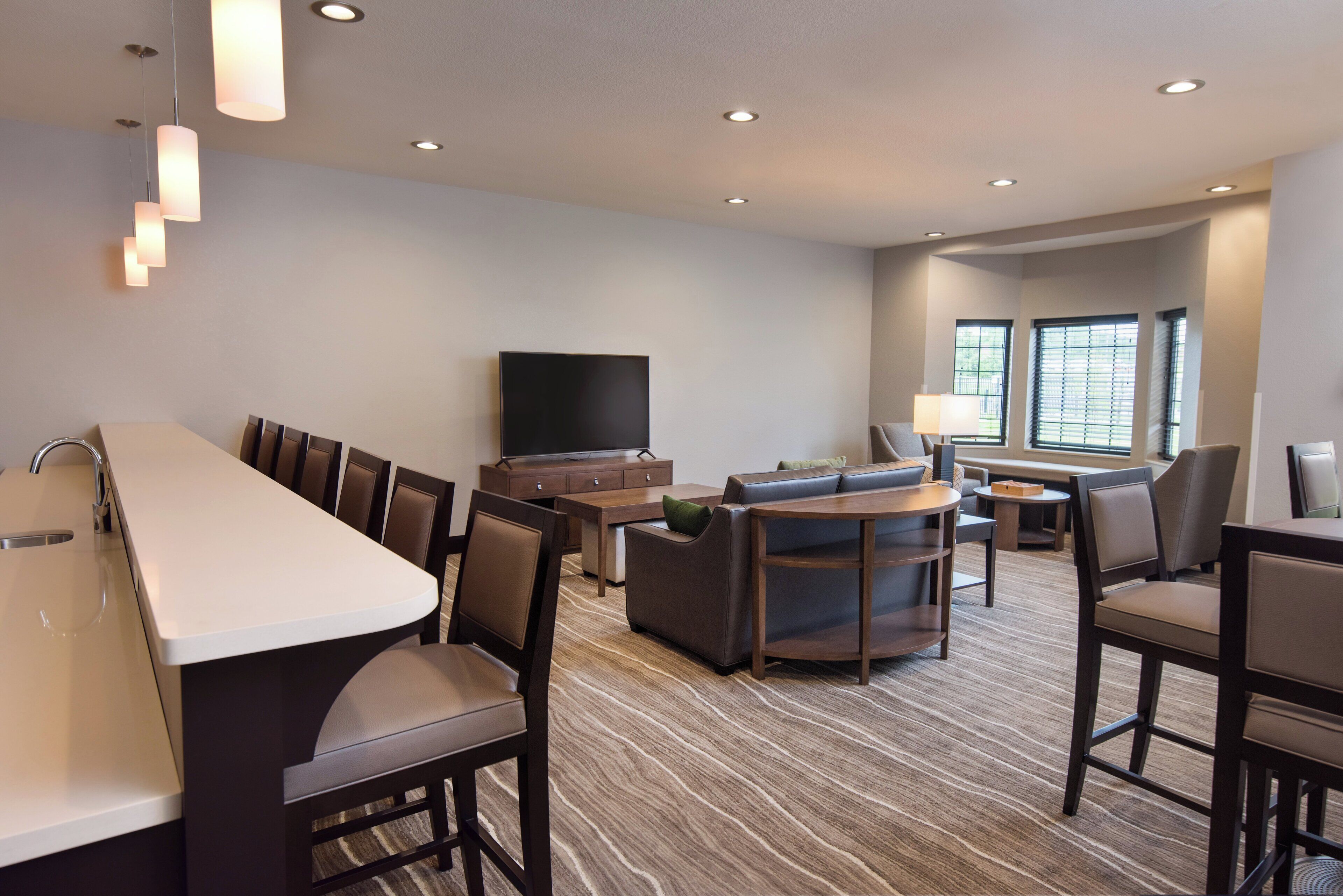 A hotel room with a kitchenette, seating area, flat-screen TV, and large windows.