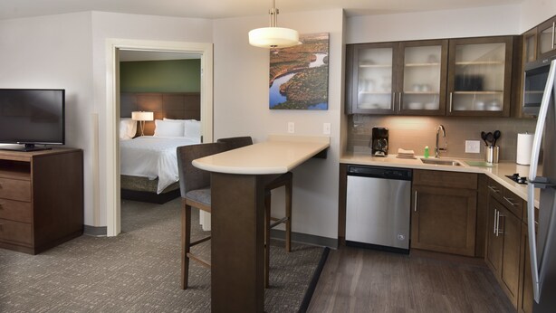Quarto de hotel compacto com cozinha compacta, uma cama com cabeceira, televisão e um quadro na parede.
