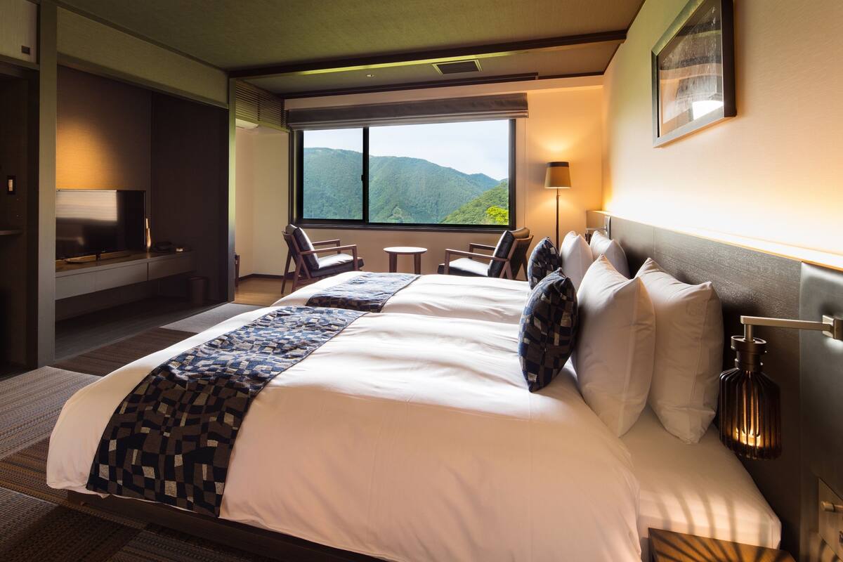Habitación de hotel con una cama grande, un escritorio, una silla y vistas a las montañas.