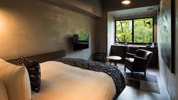 Habitación de hotel moderna con una cama grande, un televisor de pantalla plana en la pared, una mesita, una silla y una ventana con vistas a zonas verdes.