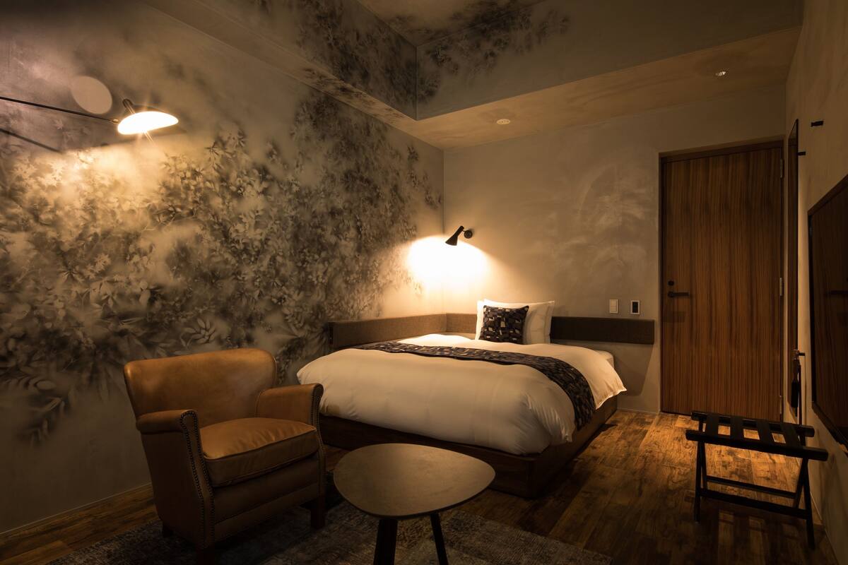Un dormitorio moderno con una cama grande, un sillón de cuero, una mesita redonda y una puerta de madera.