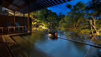 A serene outdoor pool area with a wooden deck and lounge chairs, surrounded by lush trees and a night sky.