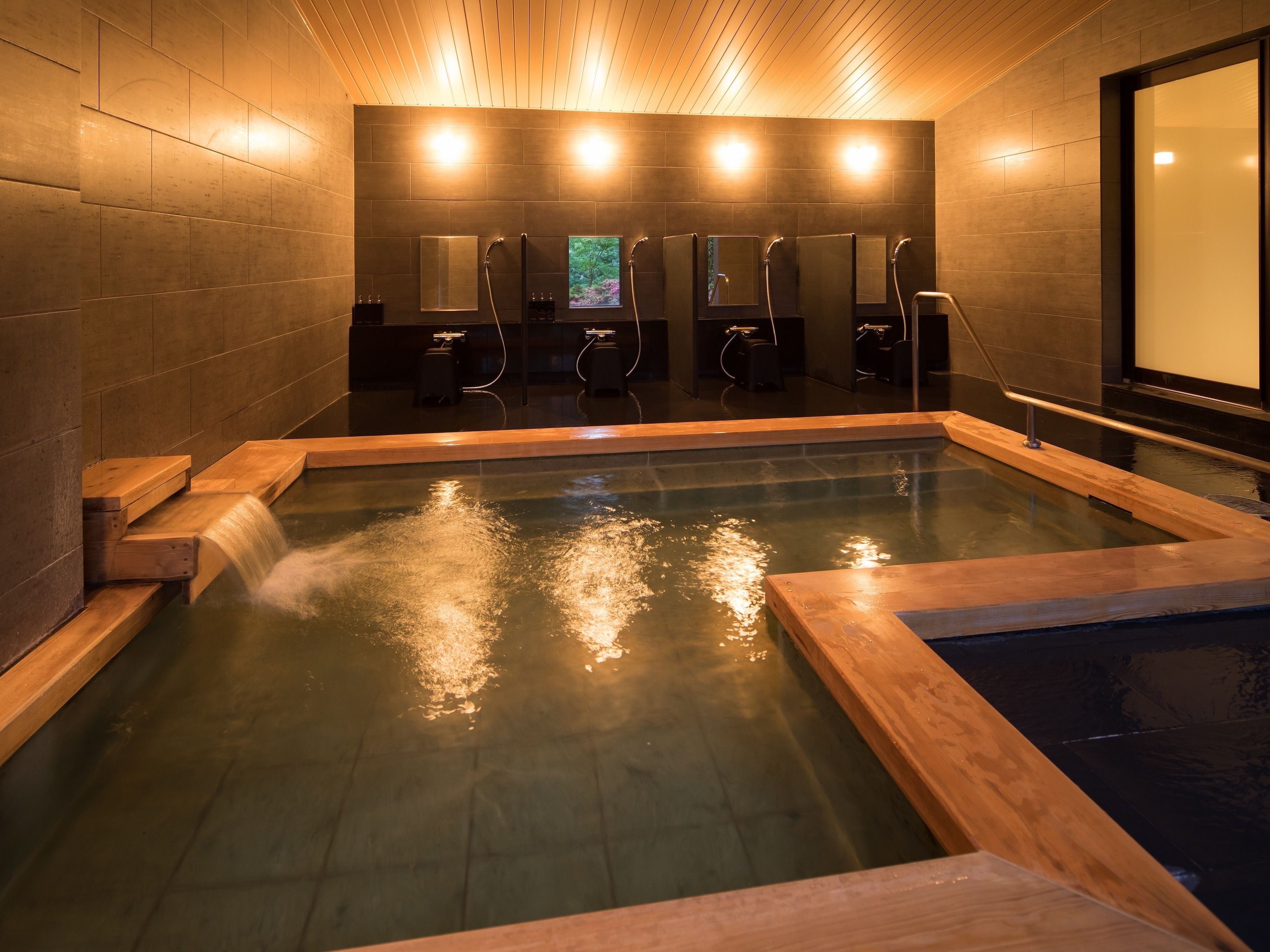 A modern spa with a large hot tub, wooden benches, and multiple shower areas.