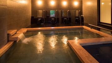 A modern spa with a large hot tub, wooden benches, and multiple shower areas.