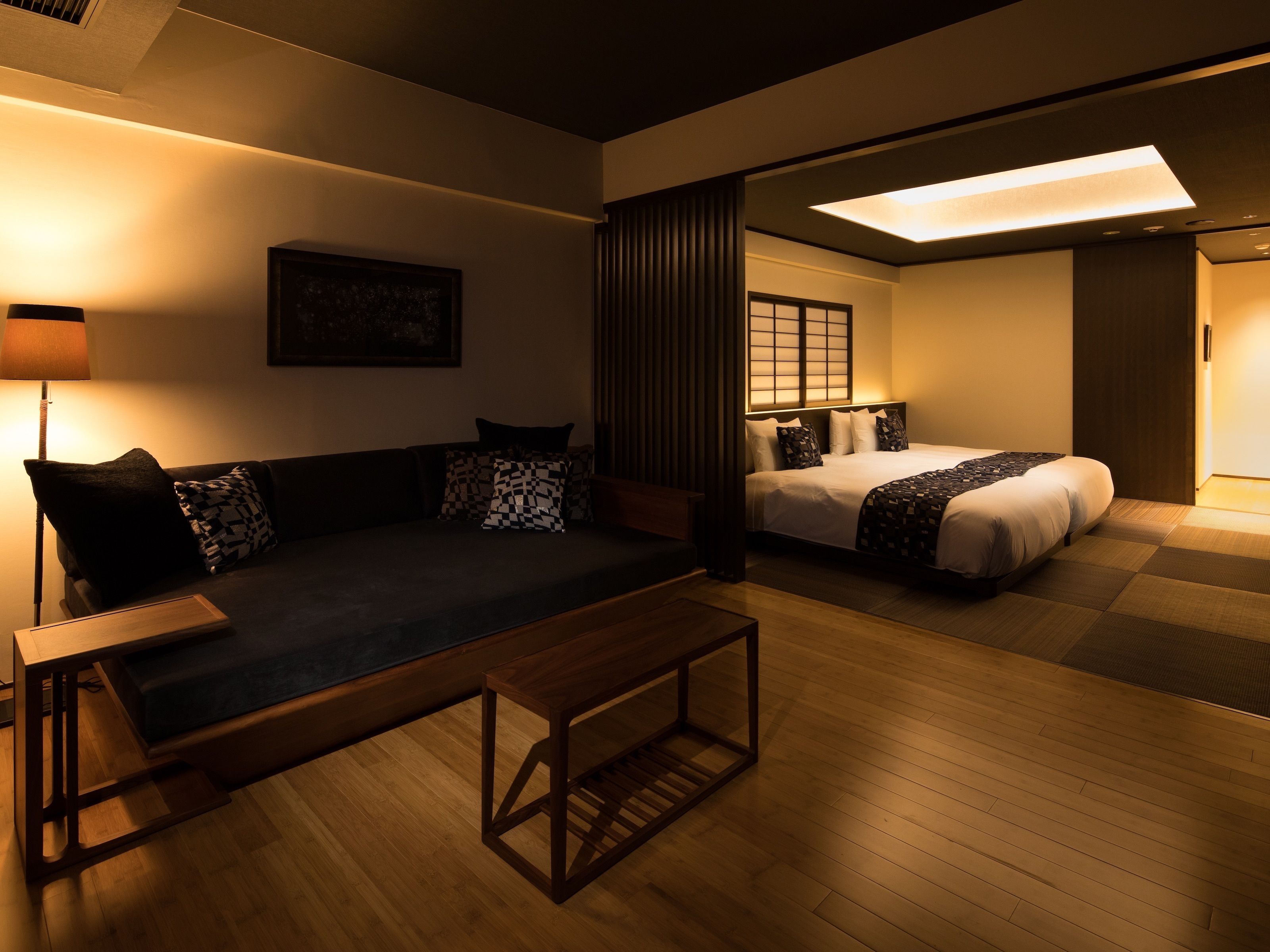 A modern hotel room with a sofa, a bed, and a wooden coffee table.
