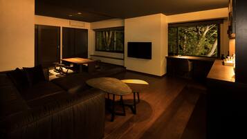 A modern living room with a dark leather sofa, a small round table, and a large window with a view of trees.