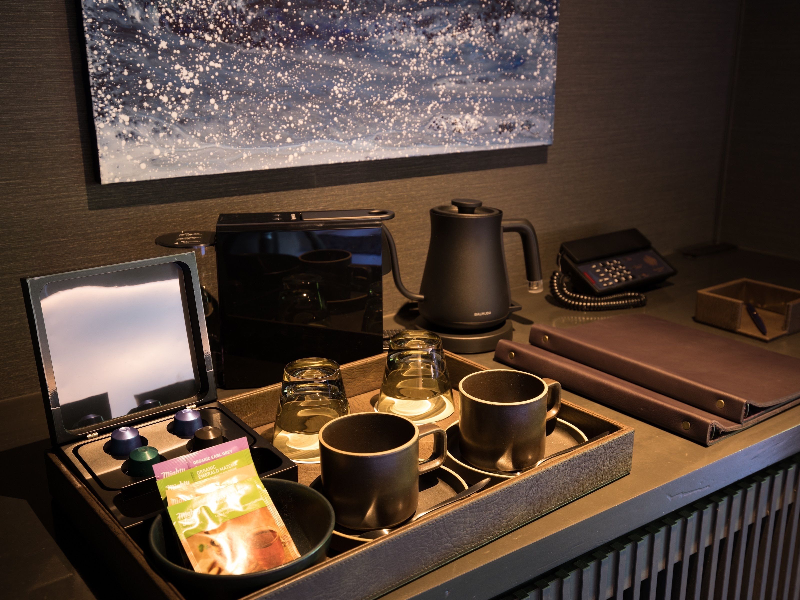 A kitchen counter with a coffee maker, kettle, and a tray with cups and a magazine.
