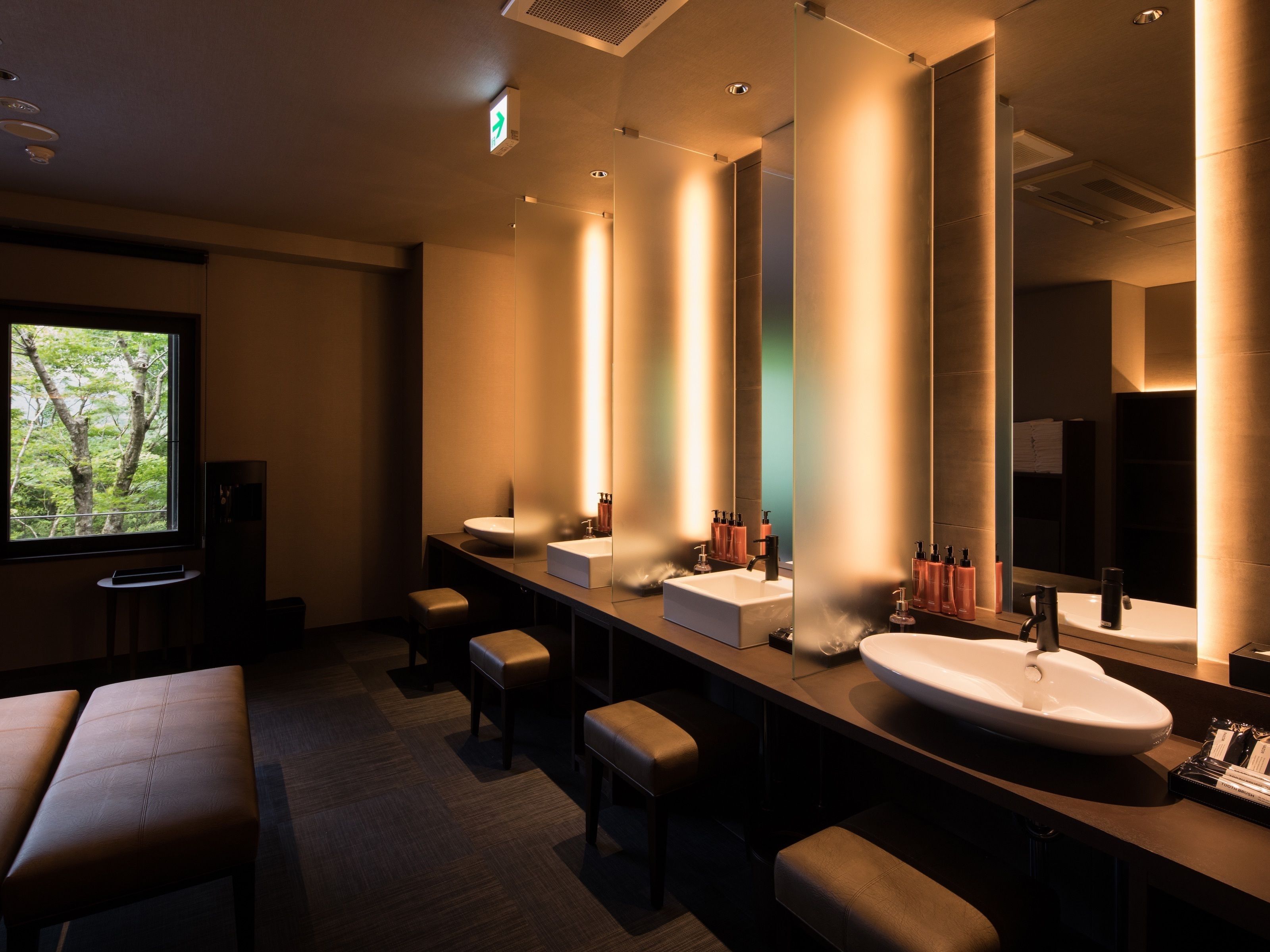 A modern bathroom with multiple sinks, benches, and a large mirror.