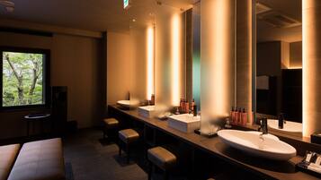 A modern bathroom with multiple sinks, benches, and a large mirror.