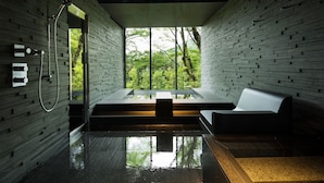 Et moderne spa med et glasomkranset jacuzzi, et bruseområde og et siddeområde med udsigt til frodig vegetation.