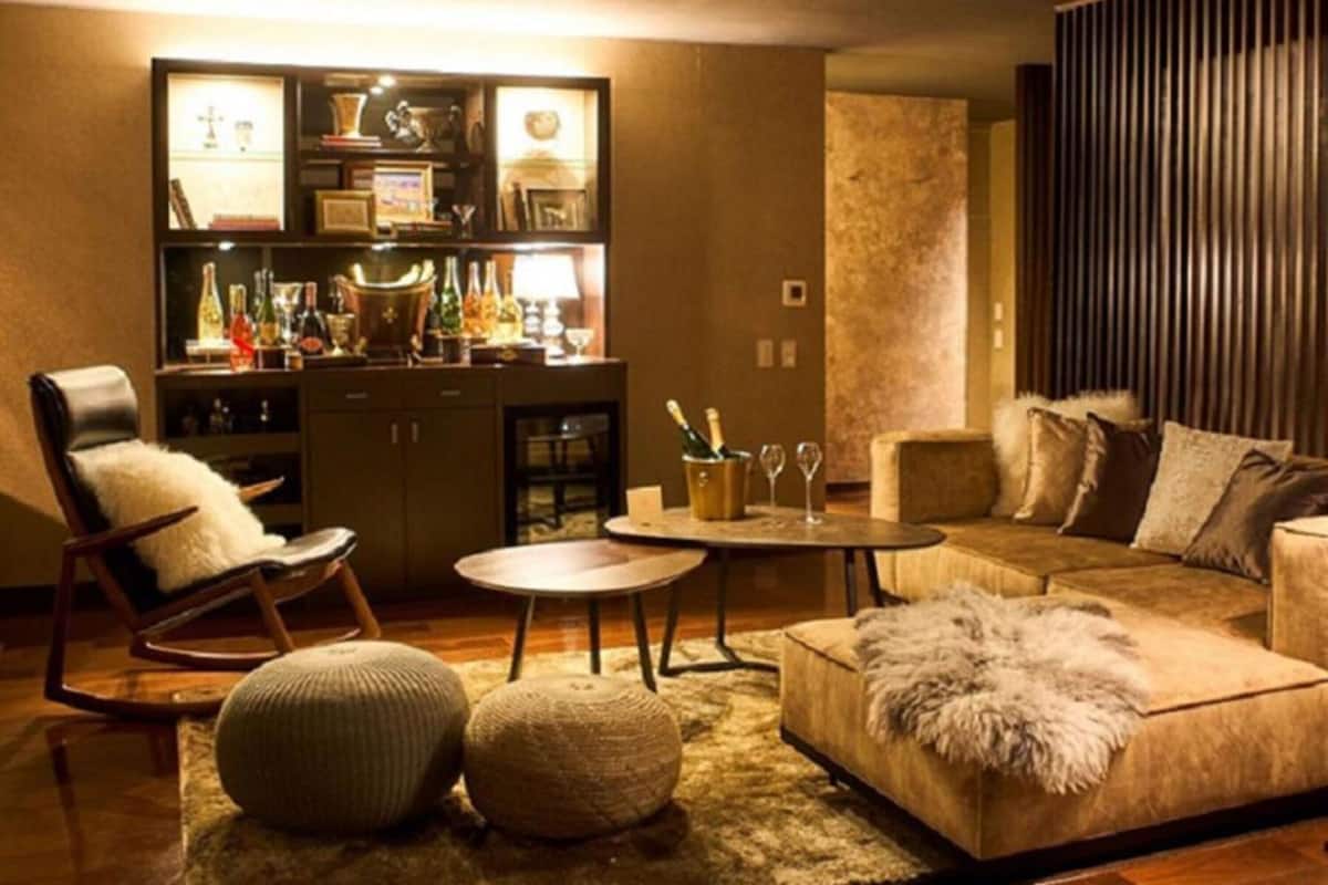 Una sala de estar acogedora con sofá, sillón y reposapiés, una mesita de centro pequeña y una zona de bar con botellas y vasos.