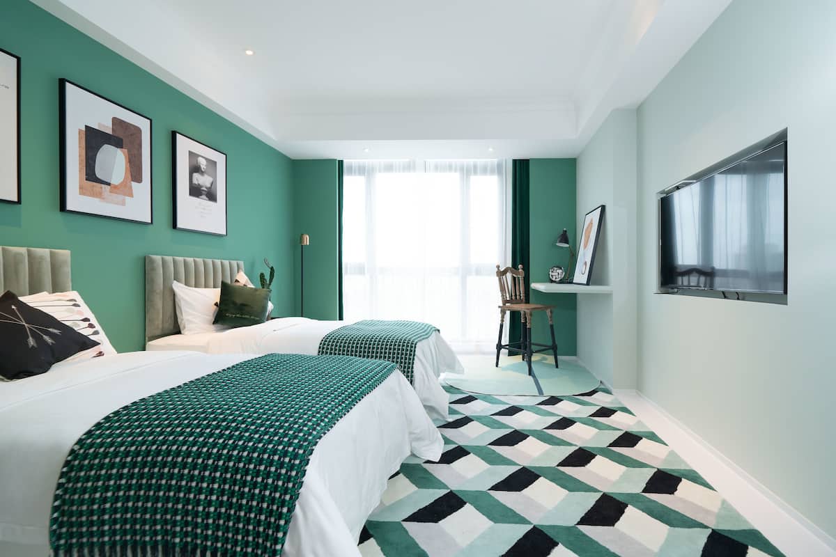 A hotel room with two beds, a large window, and artwork on the walls.