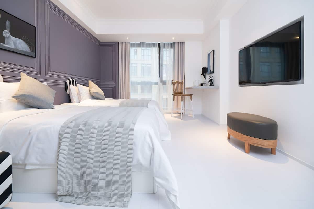 A modern bedroom with two beds, a wooden bench, and a large window.