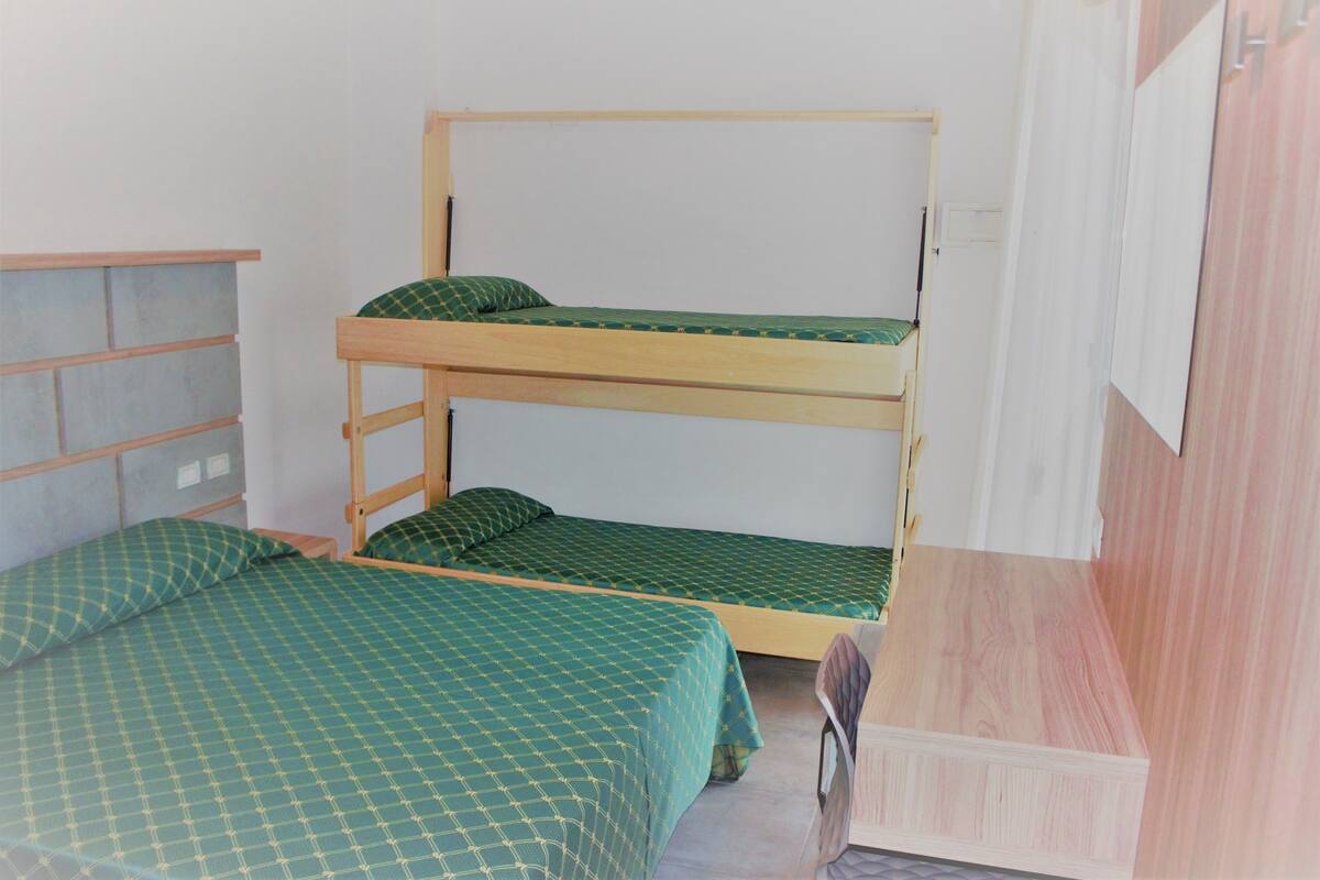 Una stanza con un letto a castello, una testiera in legno, una coperta a quadri verdi e una scrivania in legno con una sedia.