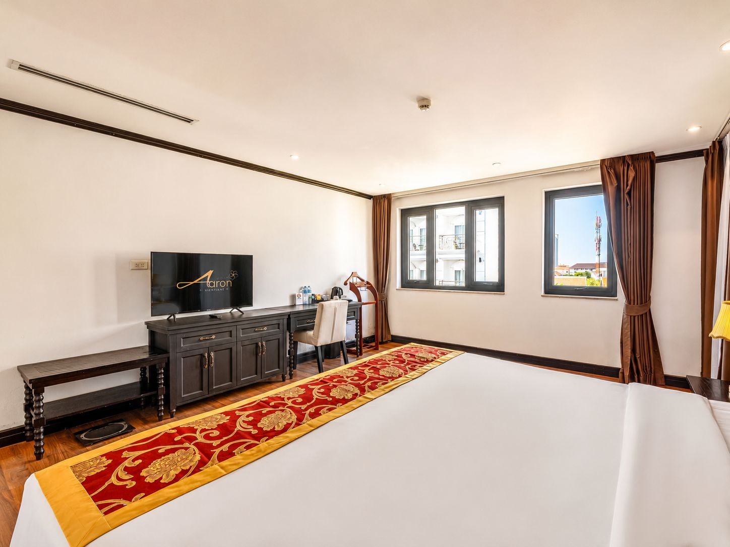 A hotel room with a large bed, a TV, a desk, and a window with curtains.