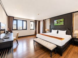 Habitación de hotel con una cama grande, un escritorio, una silla y vistas a la ciudad a través de las ventanas.