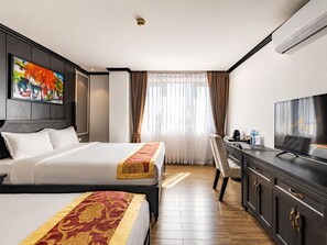 Una habitación de hotel con cama, escritorio, televisión y ventana con cortinas.