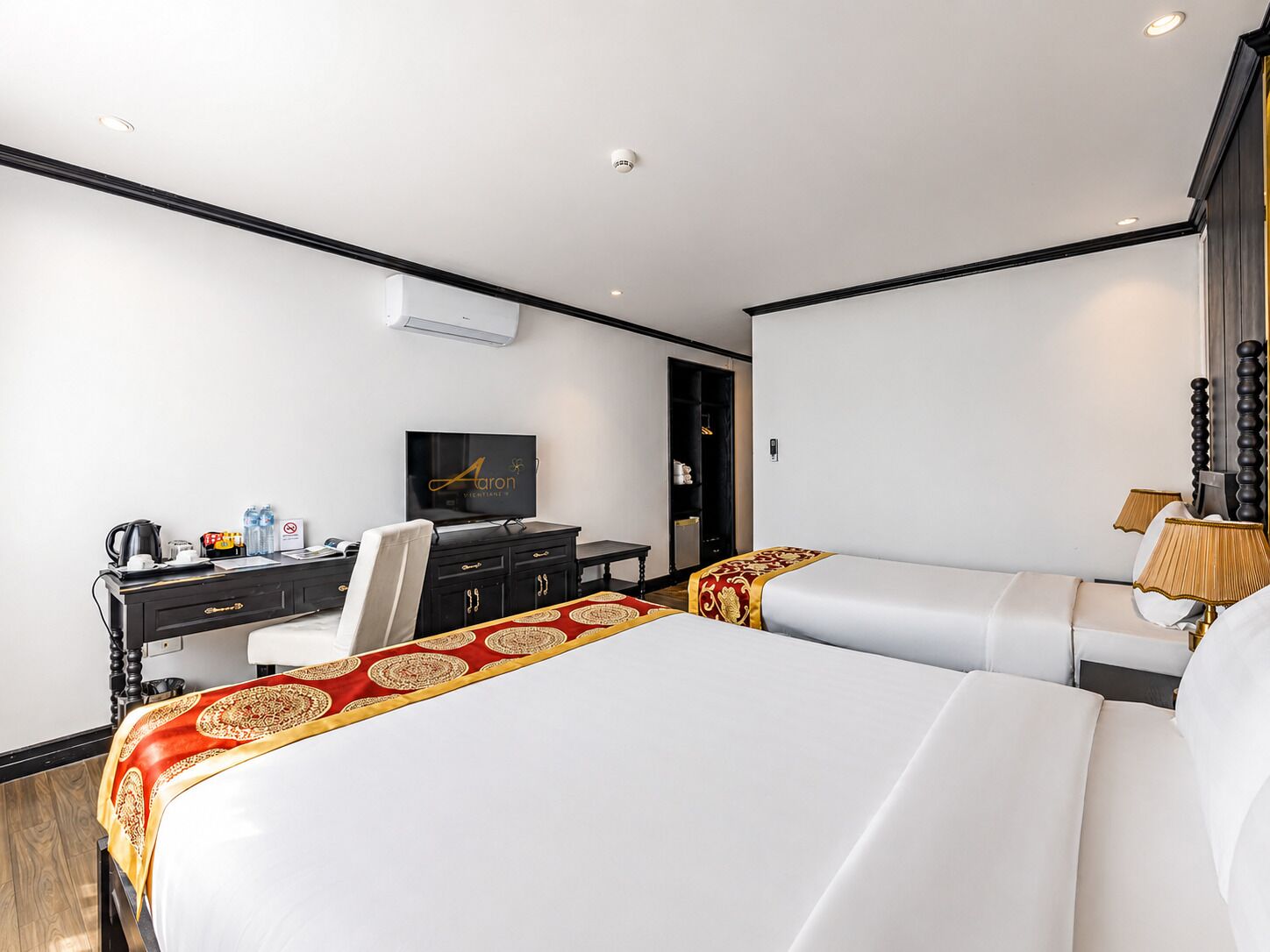 A hotel room with two beds, a desk with a television, and a minibar.