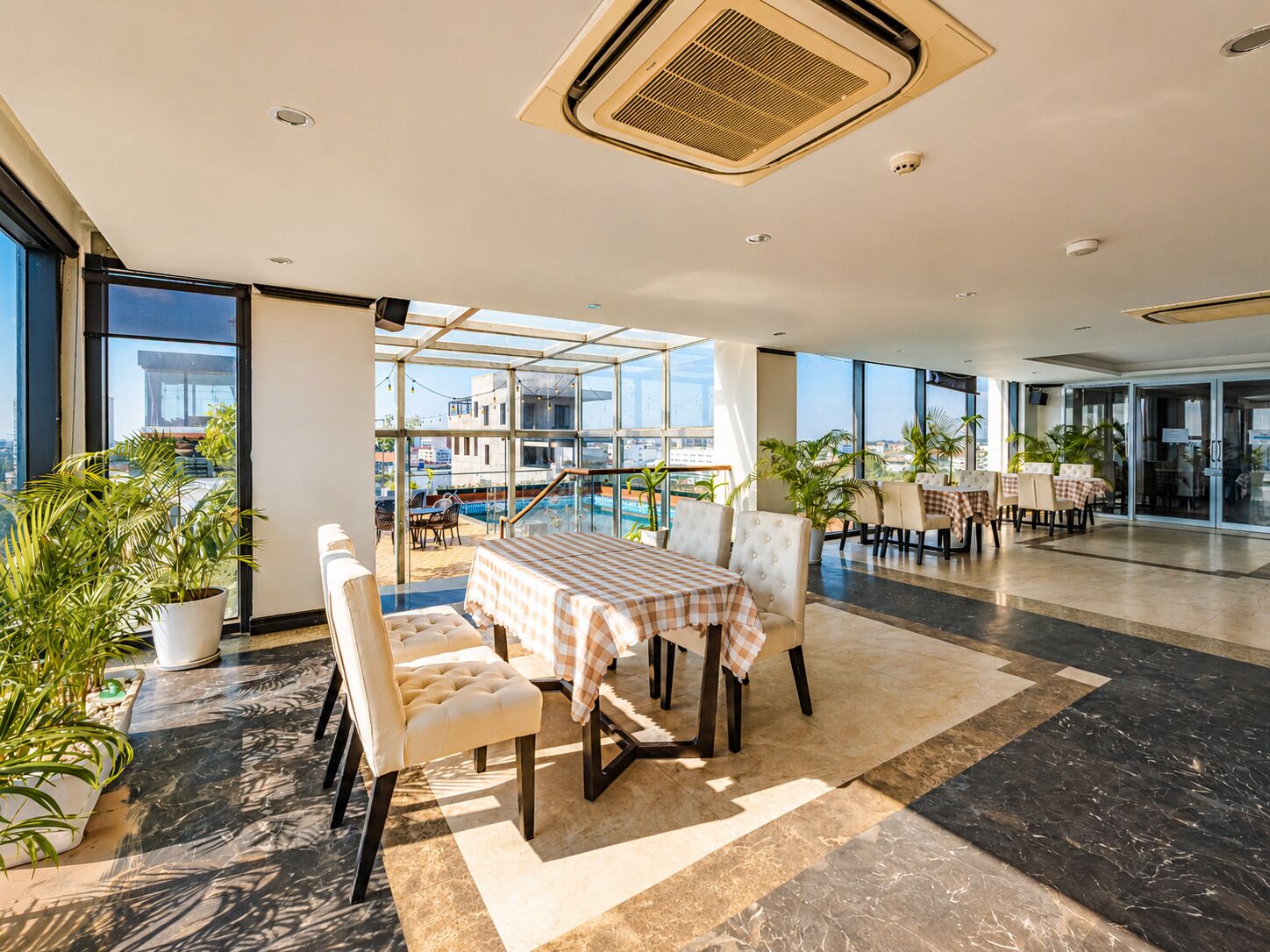 A spacious indoor area with a pool view, a dining area with checkered tablecloths, and potted plants.