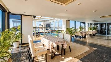 A spacious indoor area with a pool view, a dining area with checkered tablecloths, and potted plants.