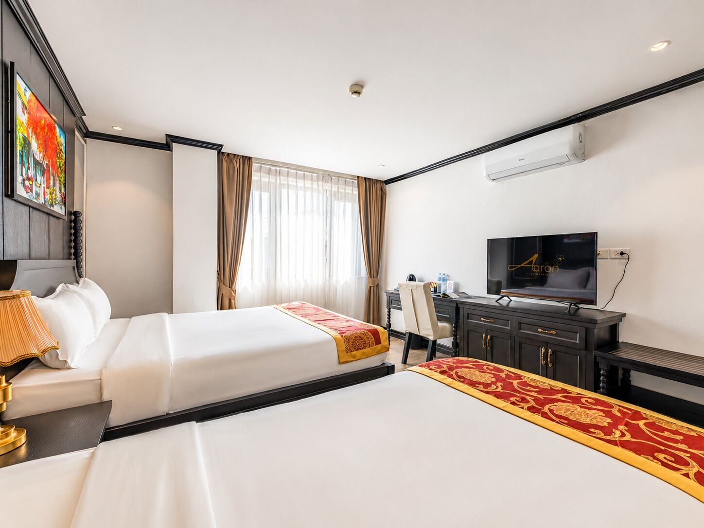 A hotel room with two beds, a desk, a television, and a window with curtains.