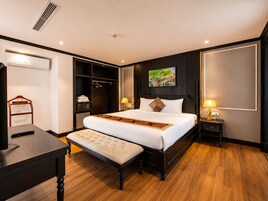A hotel room with a large bed, bedside tables, a wardrobe, and a desk with a remote control.