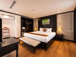 Una habitación de hotel con una cama grande, mesitas de noche, un armario y un escritorio con un control remoto.