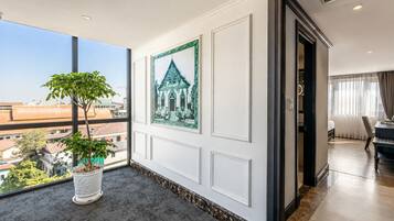 A hotel room with a large window, a potted plant, a framed picture, and a view of the cityscape.