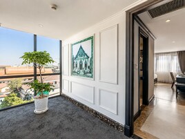 Habitación de hotel con un ventanal grande, una planta en maceta, un cuadro enmarcado y vistas de la ciudad.