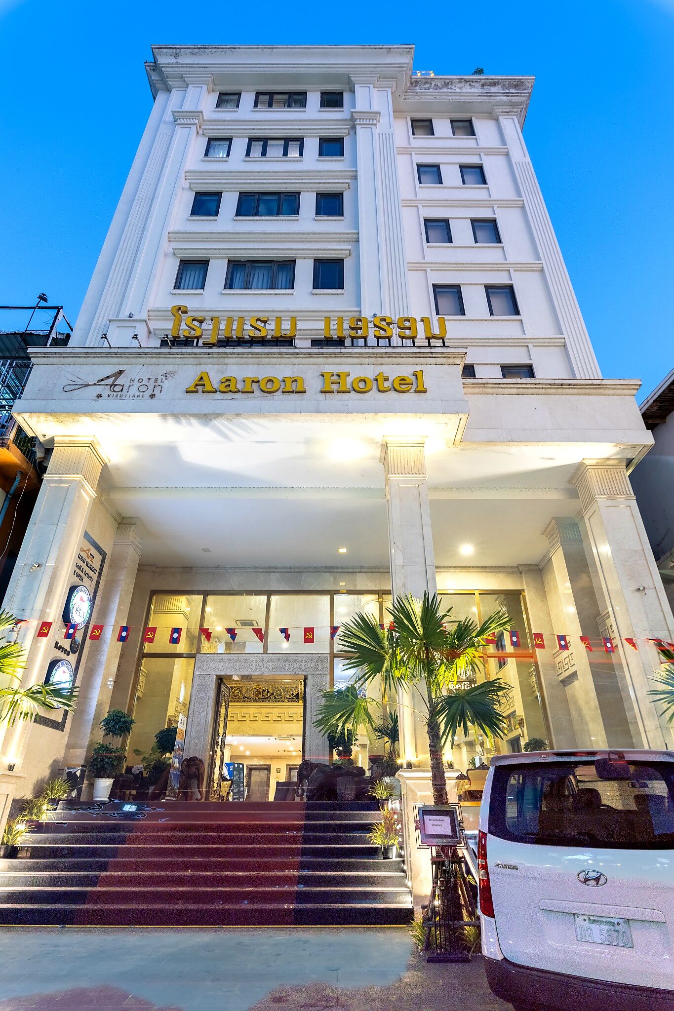 A hotel entrance with a grand facade, a staircase leading up to the entrance, and a vehicle parked in front.