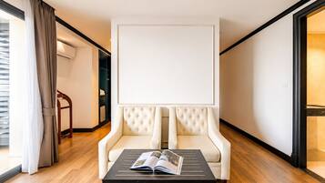 Una habitación de hotel moderna con un ventanal grande, un sillón blanco, una mesa negra con una revista, y piso de madera.