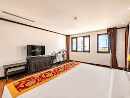 Habitación de hotel con una cama grande, televisión, escritorio y ventana con cortinas.