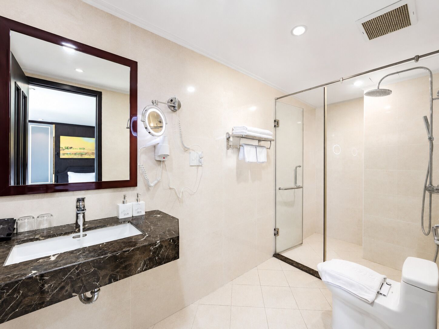 A modern bathroom with a marble sink, a large mirror, a hairdryer, and a glass-enclosed shower.